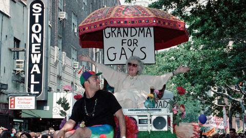 Beim CSD in New York 1989 sitzt eine ältere Dame unter einem Schild mit der Aufschrift "Grandma for Gays" und winkt den anderen Teilnehmern der Parade zu. Beim CSD in New York 1989 sitzt eine ältere Dame unter einem Schild mit der Aufschrift "Grandma for Gays" und winkt den anderen Teilnehmern der Parade zu.