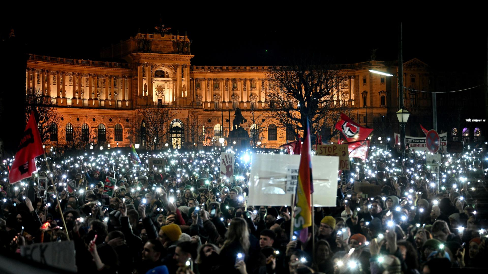 Bei einer Kundgebung stehen Menschen mit Plakaten und erhobenen Handytaschenlampen vor dem erleuchteten Bundeskanzleramt. 