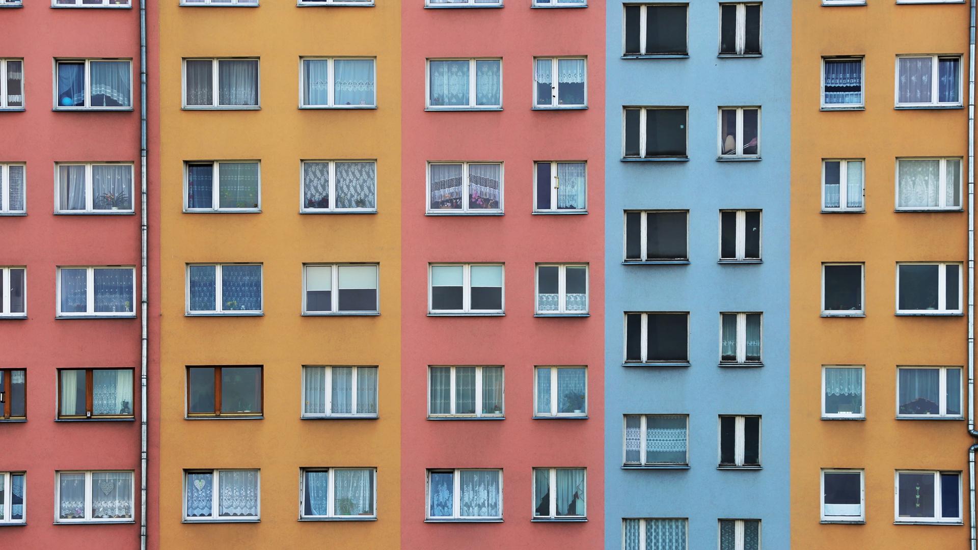 Mehrfarbige Fassade eines Wohnhauses mit zahlreichen Fenstern.