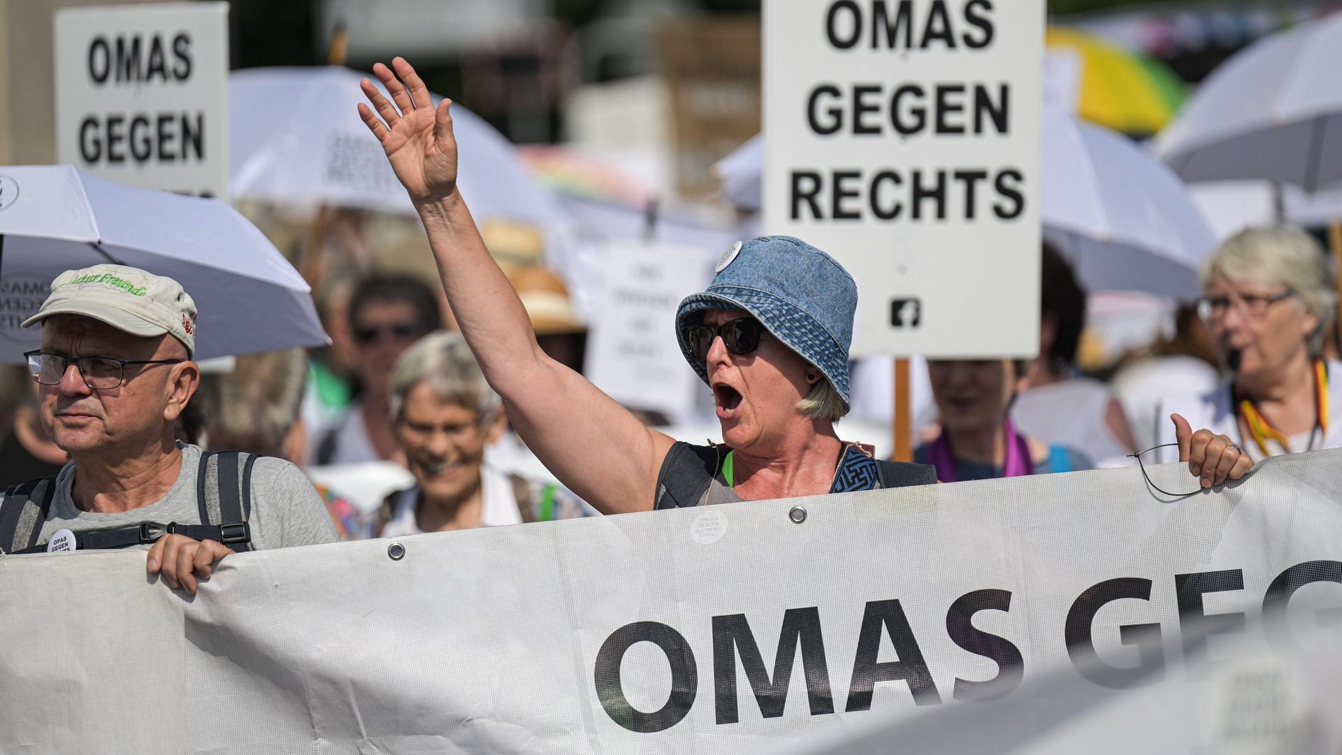 Demonstrationsteilnehmer halten Transparente mit der Aufschrift "Omas gegen rechts". Eine Frau hebt die Hand und ruft etwas.