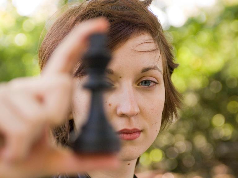 Porträt von Elisabeth Pähtz als Junioren-Weltmeisterin im Schach. Sie hält sich eine Schafigur vor das linke Auge und schaut dabei sehr ernst.