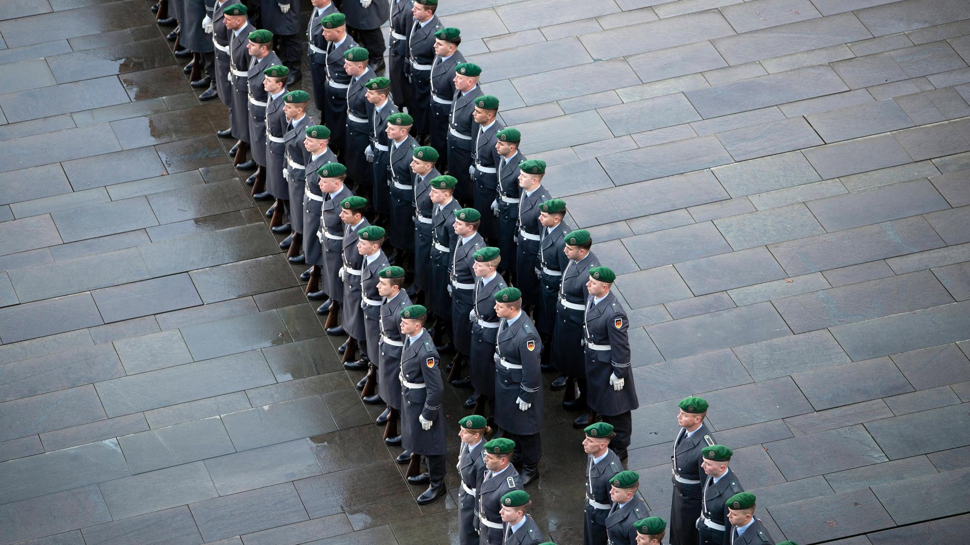 Drei Reihen von Soldaten eines Wachbataillons stehen auf grauem Pflaster. Drei Reihen von Soldaten eines Wachbataillons stehen auf grauem Pflaster.