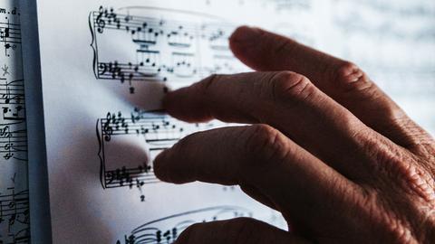 Eine Männerhand berührt vorsichtig mit den Fingerspitzen Noten, die auf einem Pult liegen.