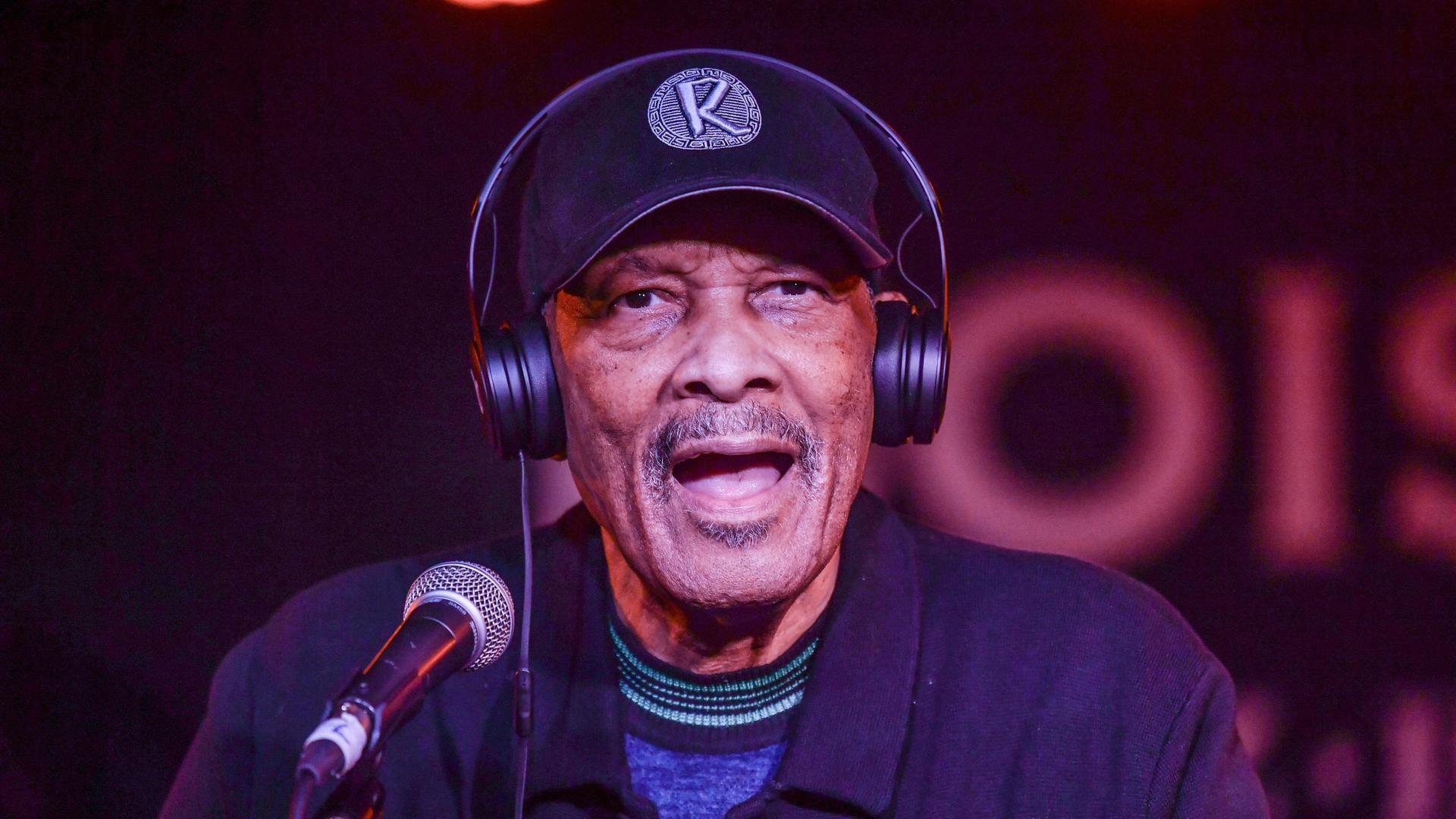 Roy Ayers hat Kopfhörer auf und spricht in ein Mikrofon.