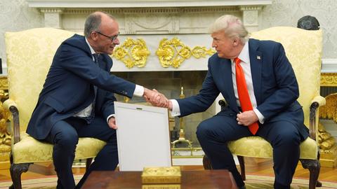 Bundeskanzler Friedrich Merz und US-Präsident Donald trump sitzen auf gelben Sesseln und schütteln sich die Hände.
