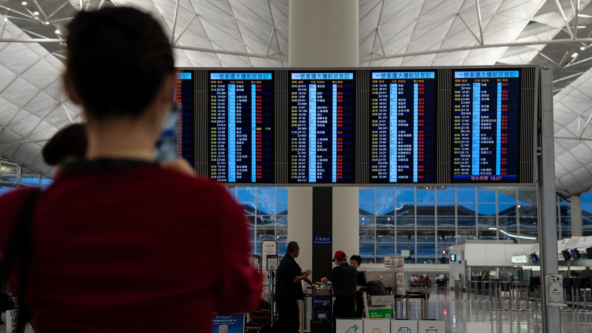 Personen schauen am Flughafen Hongkong auf ein Display, das über Flüge informiert.