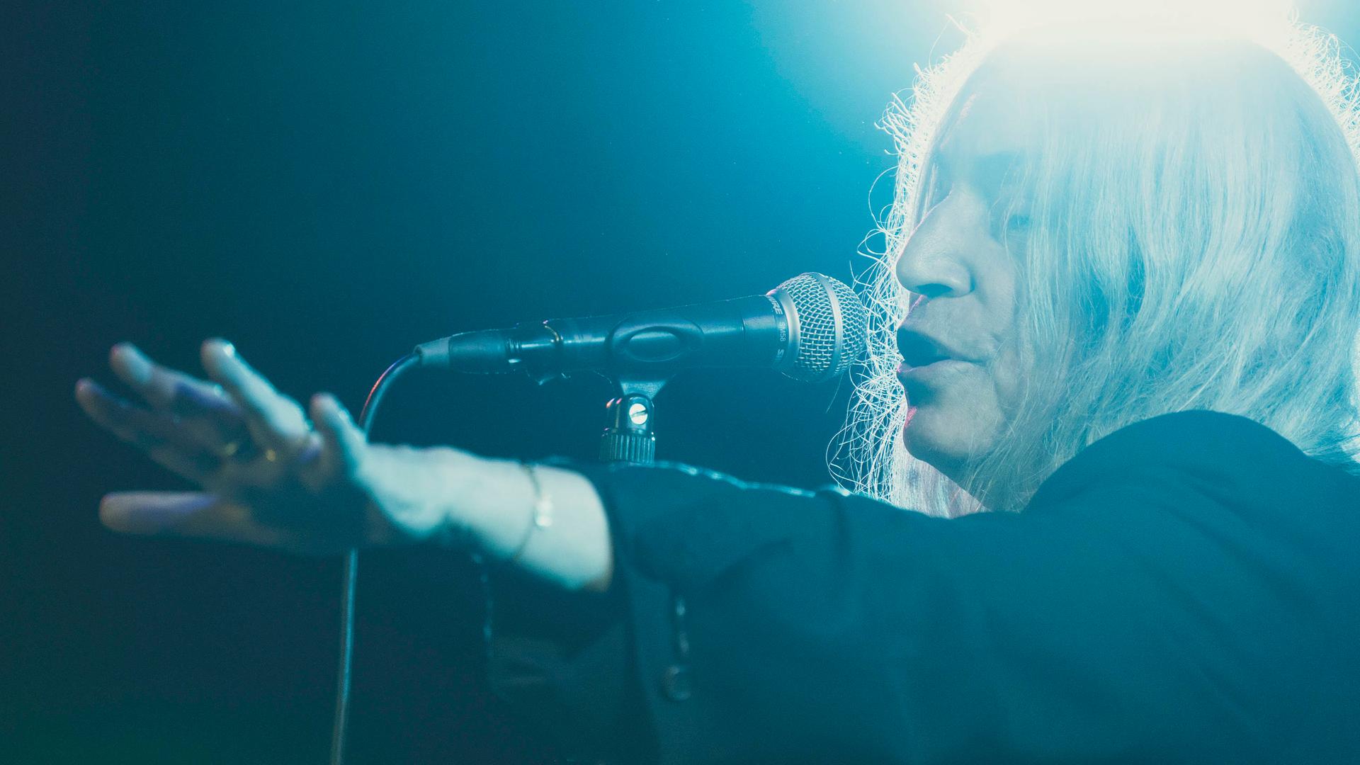 Patti Smith singt in sich versunken und in blaues Licht getaucht auf einer Bühne Patti Smith singt in sich versunken und in blaues Licht getaucht auf einer Bühne