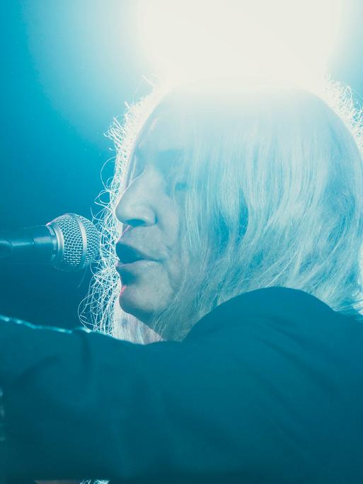 Patti Smith singt in sich versunken und in blaues Licht getaucht auf einer Bühne