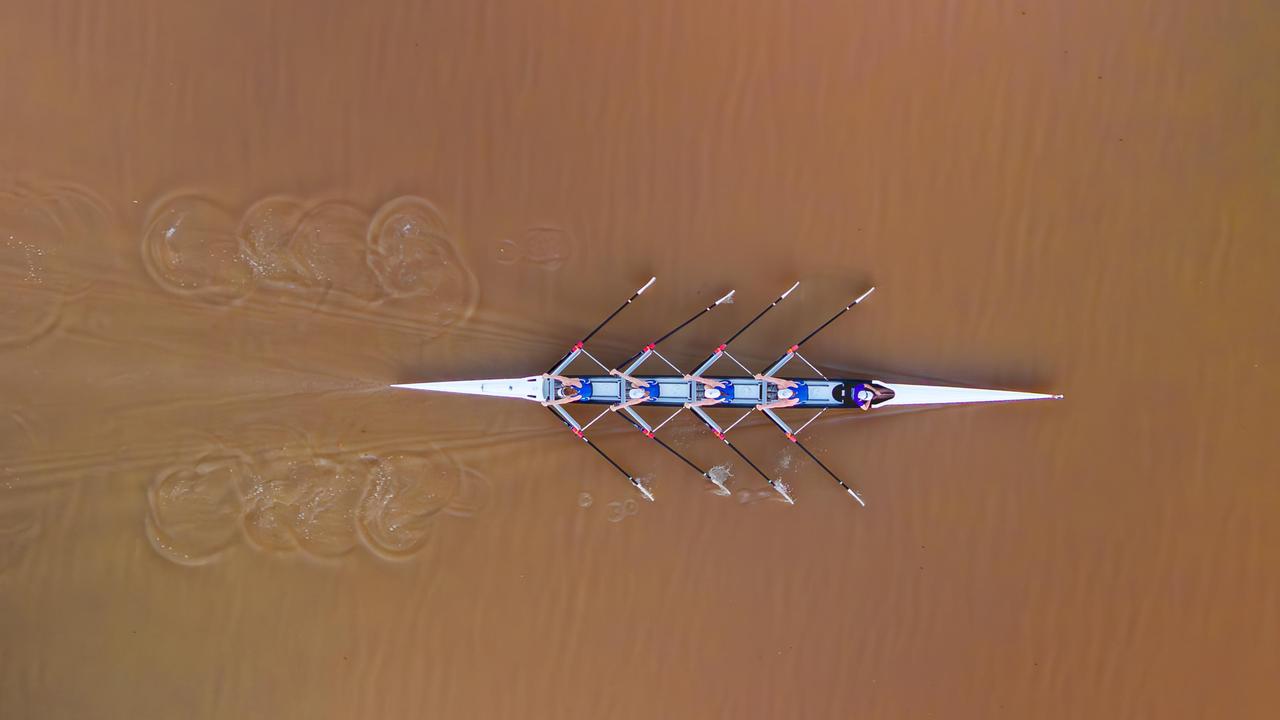 Vier Ruderer und ein Steuermann rudern auf einem Fluss.