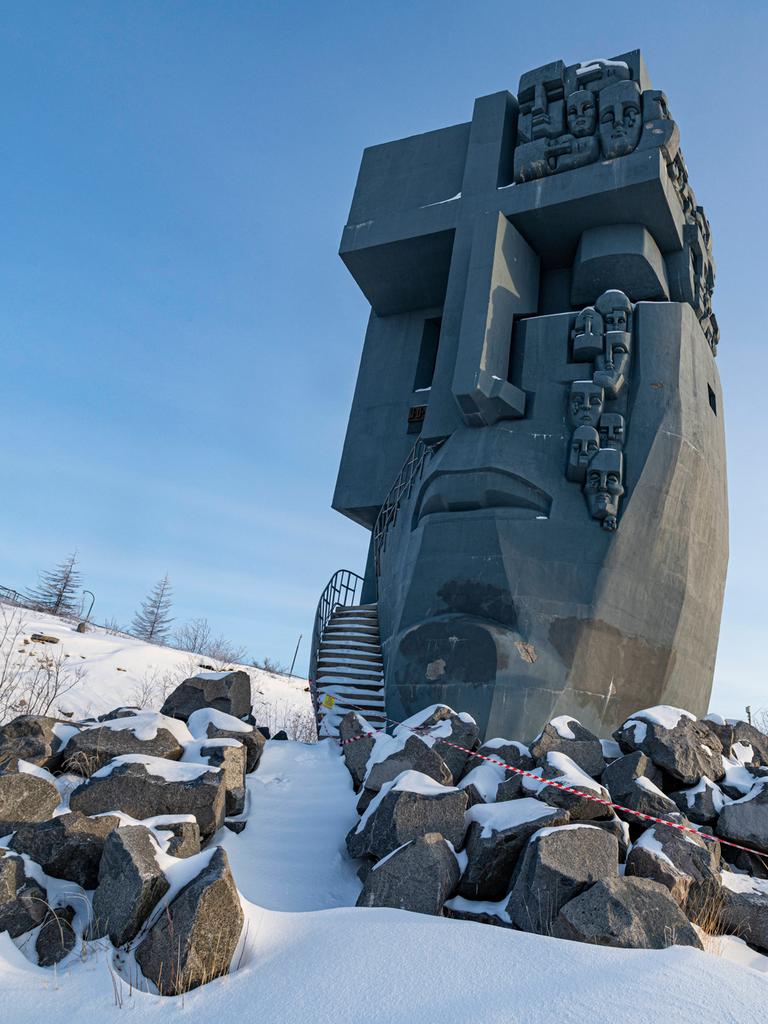 Eine großes, maskenähnliches Denkmal aus Stein mit christlichen Zeichen steht in einer Winterlandschaft.
