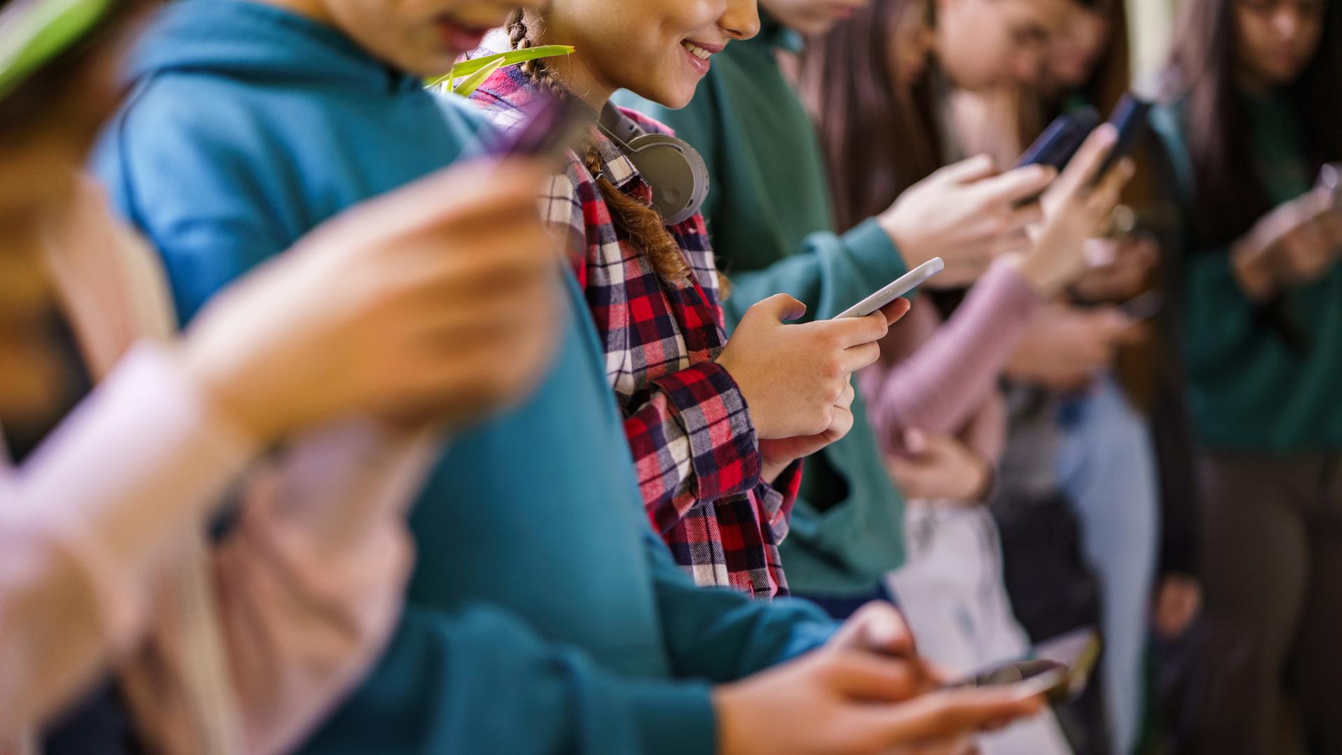 Seitenansicht einer Gruppe von Schulkindern, die in der Schule Mobiltelefone benutzen.