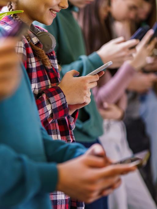 Seitenansicht einer Gruppe von Schulkindern, die in der Schule Mobiltelefone benutzen.