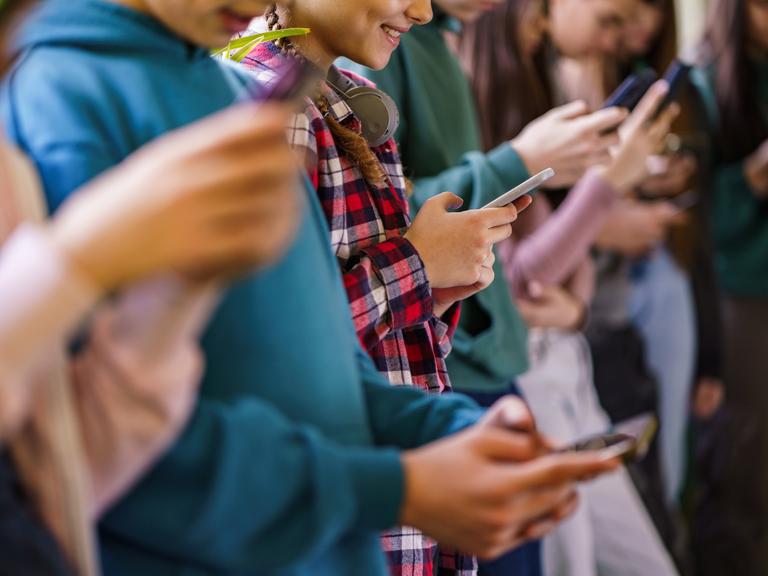 Seitenansicht einer Gruppe von Schulkindern, die in der Schule Mobiltelefone benutzen.