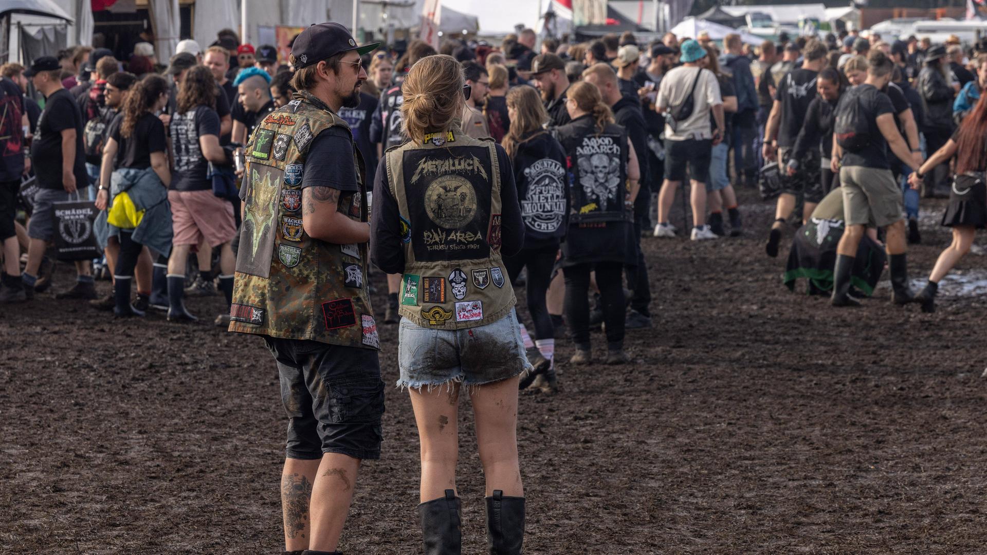 Mehrere Menschen stehen beim Wacken-Festival auf matschigem Boden. Sie tragen Heavy Metal-Kleidung. Mehrere Menschen stehen beim Wacken-Festival auf matschigem Boden. Sie tragen Heavy Metal-Kleidung.