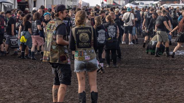 Mehrere Menschen stehen beim Wacken-Festival auf matschigem Boden. Sie tragen Heavy Metal-Kleidung.