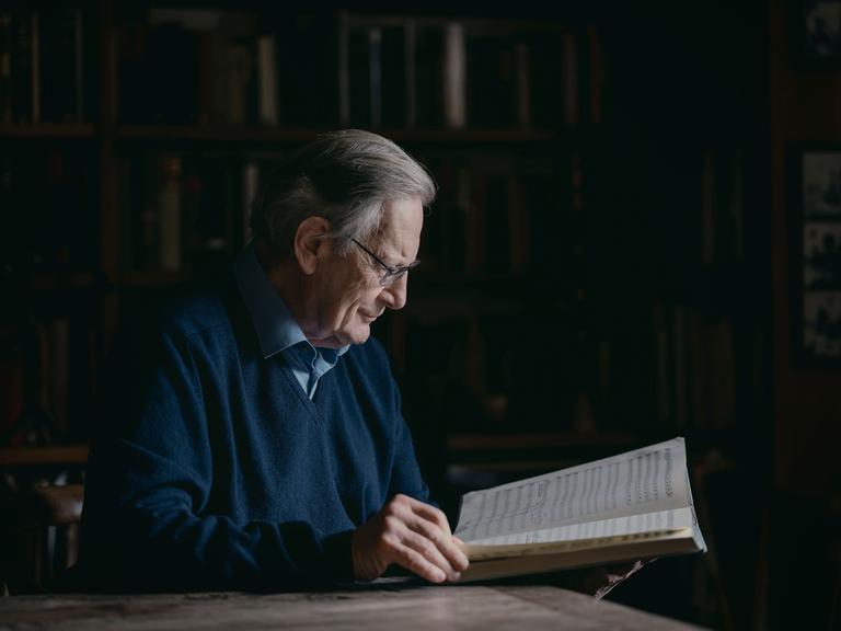 Sir John Eliot Gardiner sitzt an einem Schreibtisch und blickt in eine große, aufgeschlagene Partitur. 