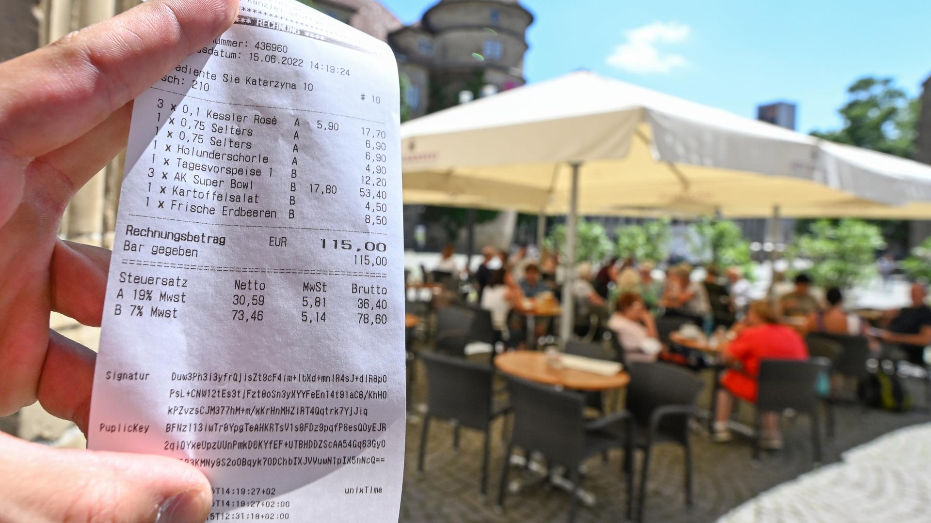 Eine Bedienung hält in einem Restaurant in Stuttgart eine Rechnung mit zwei verschiedenen Mehrwertsteuersätzen für Getränke und Speisen ion die Kamera. Im Hintergrund erkannt man eine Außengastronomie.