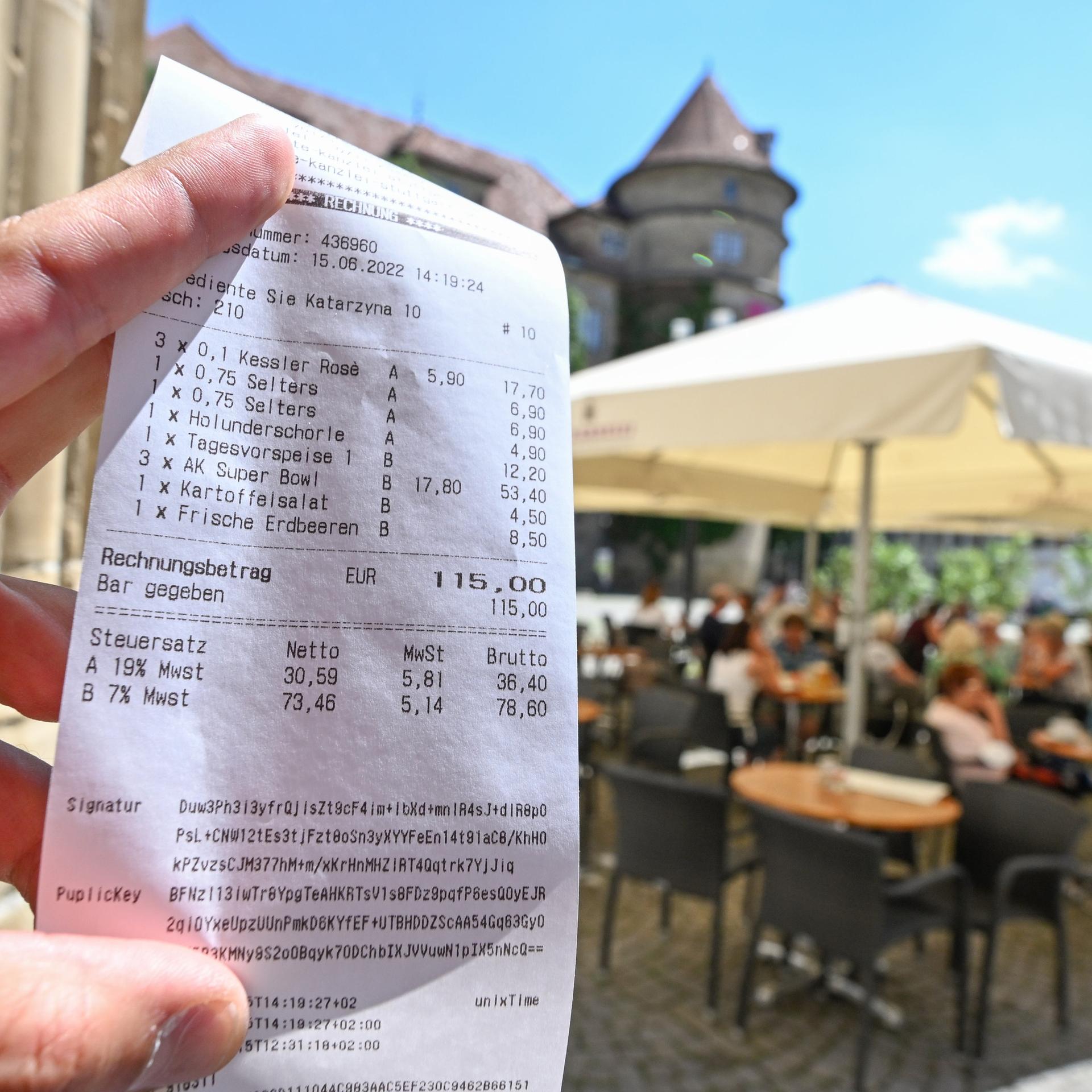 Eine Bedienung hält in einem Restaurant in Stuttgart eine Rechnung mit zwei verschiedenen Mehrwertsteuersätzen für Getränke und Speisen ion die Kamera. Im Hintergrund erkannt man eine Außengastronomie.