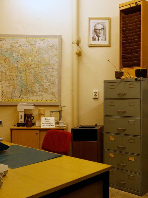 Blick in ein ehemaliges Büro mit Büromöbiliar im MfS in Leipzig, ein Bild von Honecker hängt an der Wand