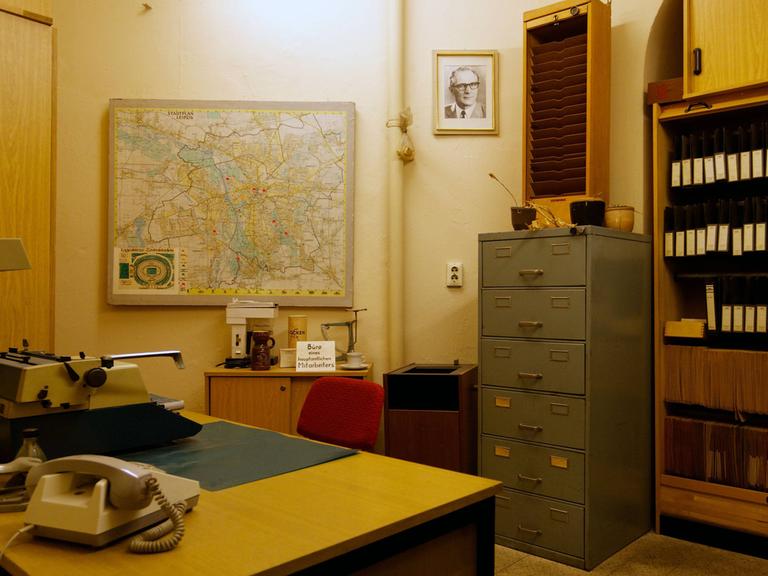 Blick in ein ehemaliges Büro mit Büromöbiliar im MfS in Leipzig, ein Bild von Honecker hängt an der Wand