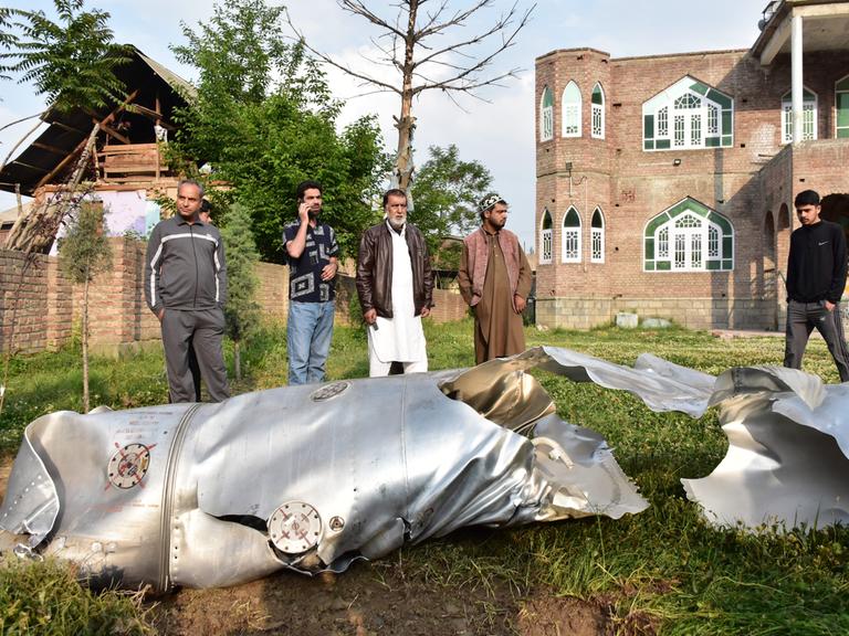 Ein paar kaschmirische Männer stehen vor zerbeulten Flugzeugteilen