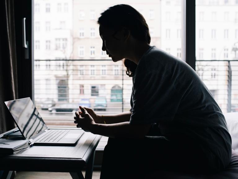 Eine junge Frau sitzt vor dem Fenster am Laptop. 