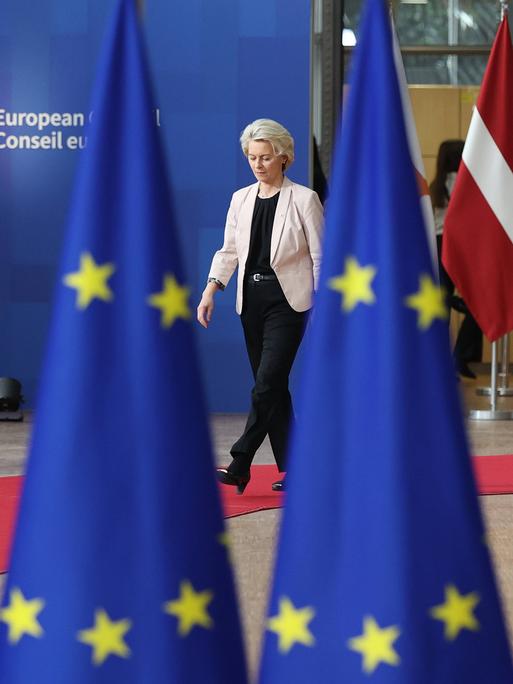 EU-Kommissionspräsidentin Ursula von der Leyen läuft auf einem roten Teppich, zwischen ihr und der Kamera stehen EU-Flaggen ( 26.10.2023)