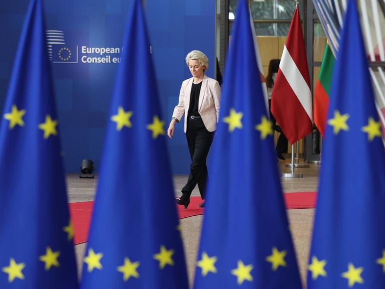 EU-Kommissionspräsidentin Ursula von der Leyen läuft auf einem roten Teppich, zwischen ihr und der Kamera stehen EU-Flaggen ( 26.10.2023)
