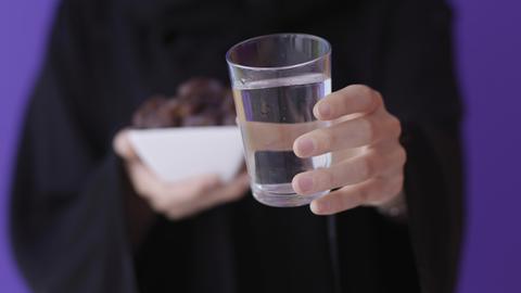 Eine muslimische Frau hält Datteln und ein Glas Wasser vor sich.