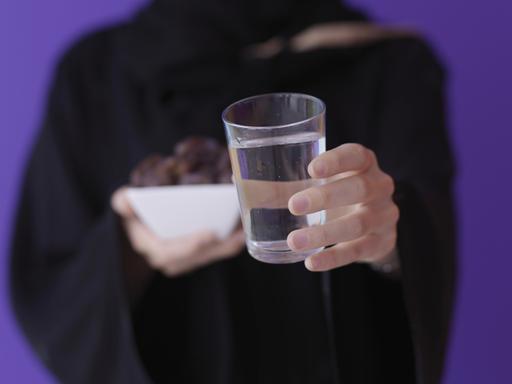 Eine muslimische Frau hält Datteln und ein Glas Wasser vor sich.