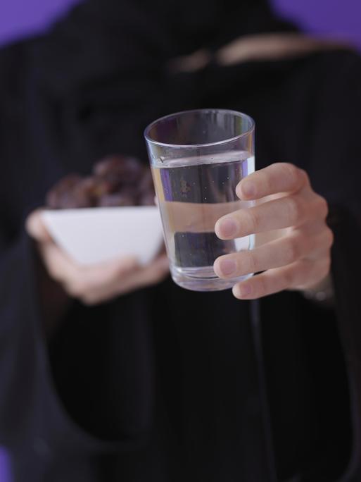 Eine muslimische Frau hält Datteln und ein Glas Wasser vor sich.