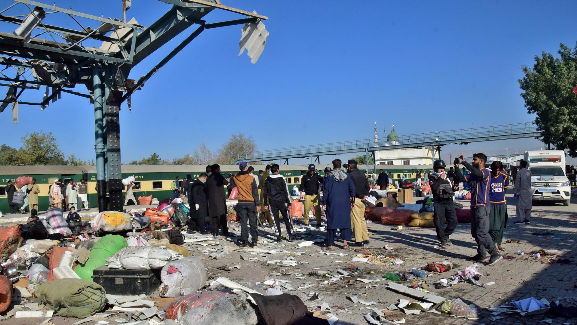 Eine Gruppe Menschen steht auf einem durch eine Explosion zerstörten Bahnsteig, überall liegen Trümmer und Gebäudeteile. Eine Gruppe Menschen steht auf einem durch eine Explosion zerstörten Bahnsteig, überall liegen Trümmer und Gebäudeteile.