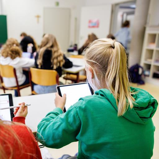 Schülerinnen einer sechsten Klasse arbeiten in einem Klassenraum an ihren Tablets.  