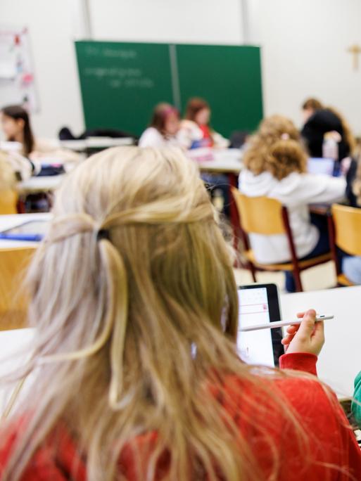 Schülerinnen einer sechsten Klasse arbeiten in einem Klassenraum an ihren Tablets.  
