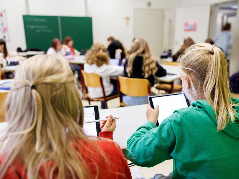 Schülerinnen einer sechsten Klasse arbeiten in einem Klassenraum an ihren Tablets.  