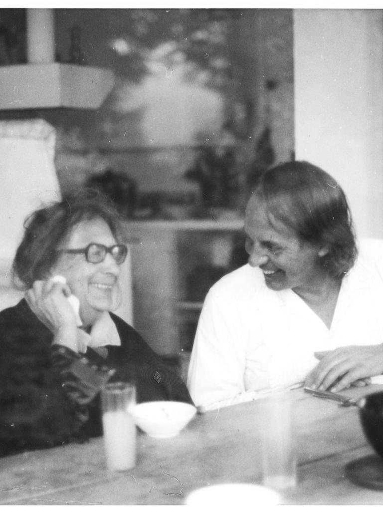 Der weiß gekleidete, jüngere Karlheinz Stockhausen sitzt neben der älteren Recha Freier, beide lachend ins Gespräch vertieft.