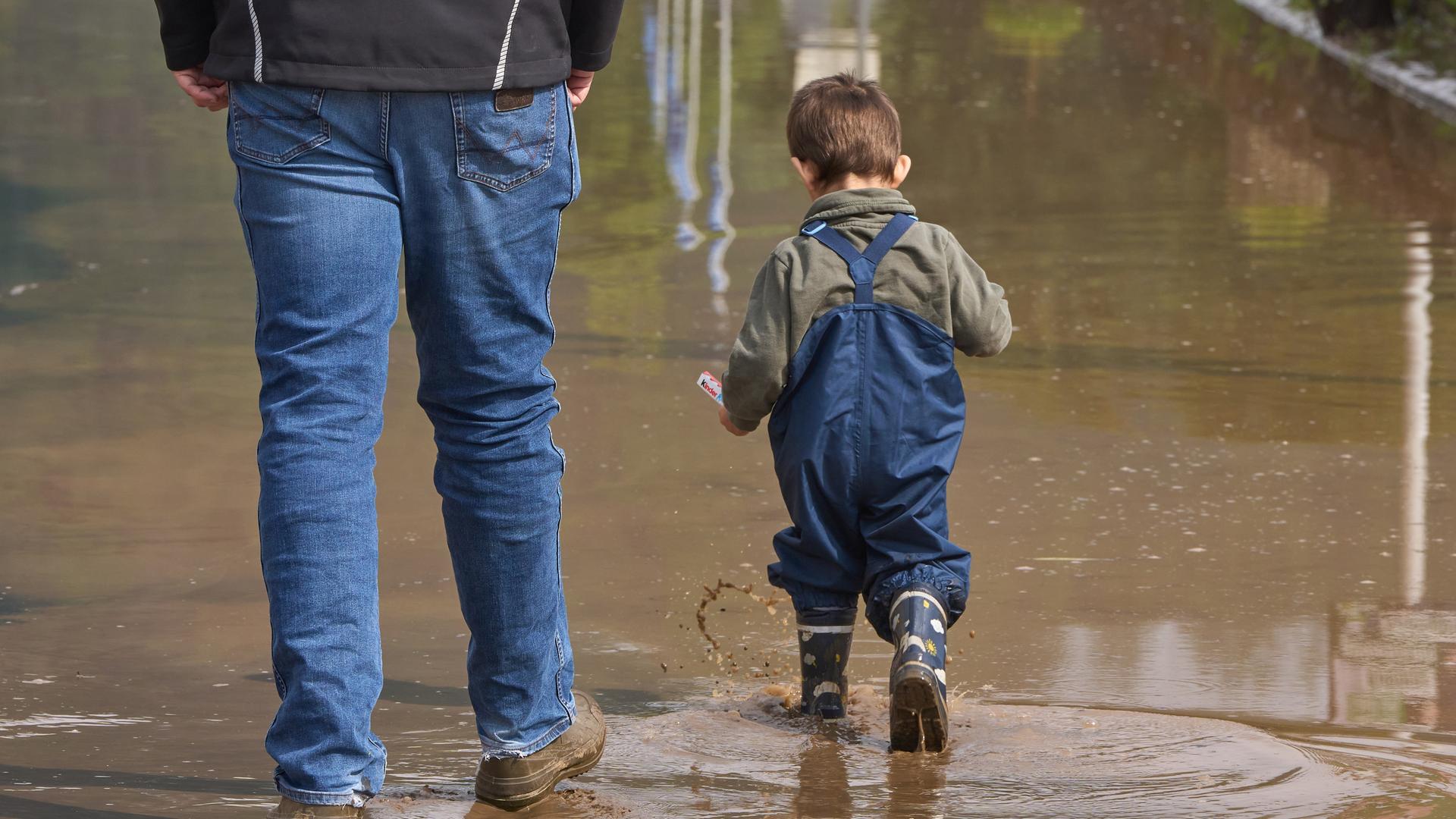 Ein Kind spaziert mit seinem Vater mit Gummistiefeln durch das Hochwasser.