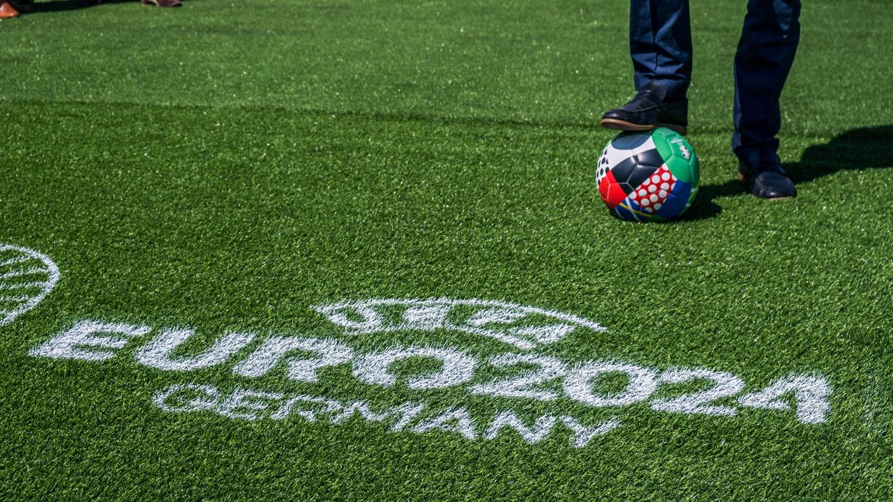 Das Bild zeigt einen Fußball-Rasen, auf dem mit weißer Farbe "UEFA EURO 2024 Germany" geschrieben ist, im Hintergrund ist der Ball für die Europameisterschaft in Deutschland zu sehen.