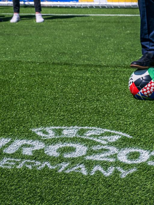 Das Bild zeigt einen Fußball-Rasen, auf dem mit weißer Farbe "UEFA EURO 2024 Germany" geschrieben ist, im Hintergrund ist der Ball für die Europameisterschaft in Deutschland zu sehen.