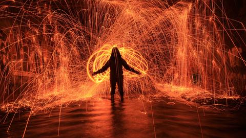 Silhouette einer Person, die Lichtspiele mit Rot und Orange macht.