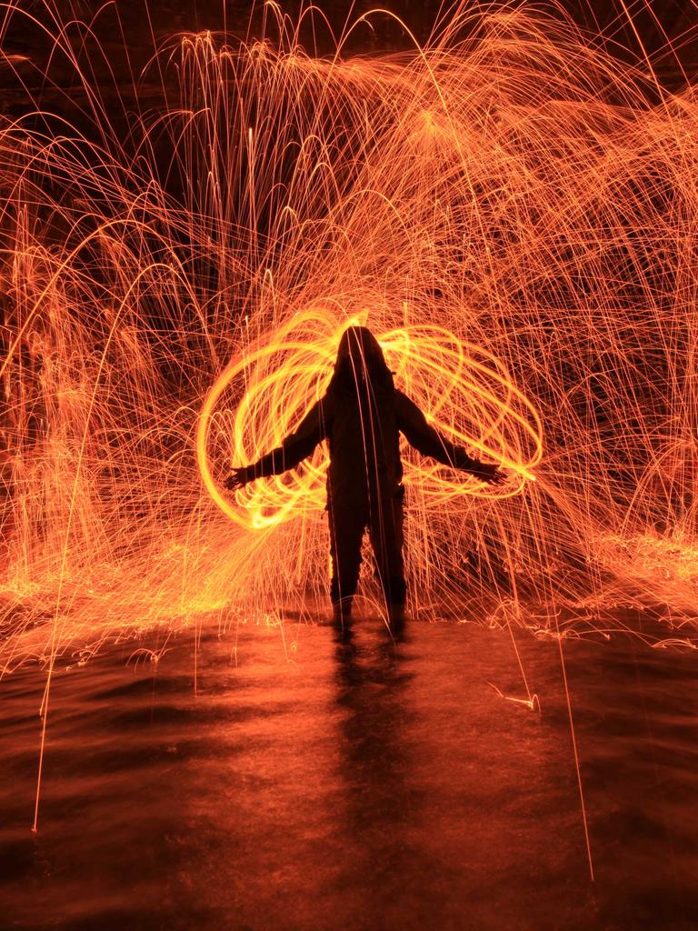 Silhouette einer Person, die Lichtspiele mit Rot und Orange macht.