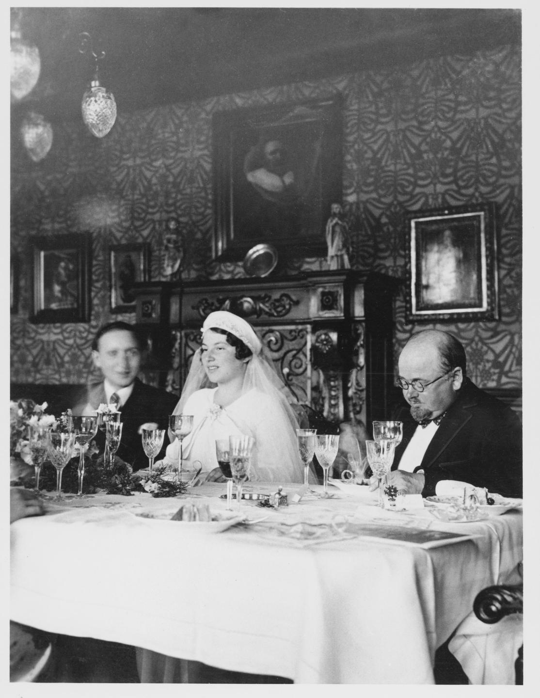 Braut und Bräutigam sitzen am Esstisch, im Hintergrund sind Gemälde zu sehen.