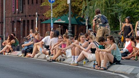 Viele junge Menschen sitzen auf dem Straßenpflaster der Berliner Hobrechtbrücke, Hot Spot, Sommer in Berlin, zwischen Berlin-Neukoelln und Berlin-Kreuzberg.