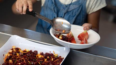 Ein Mädchen legt in einer Kantine Salat auf ihren Teller.