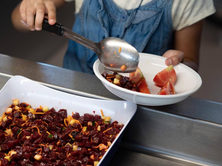 Ein Mädchen legt in einer Kantine Salat auf ihren Teller.