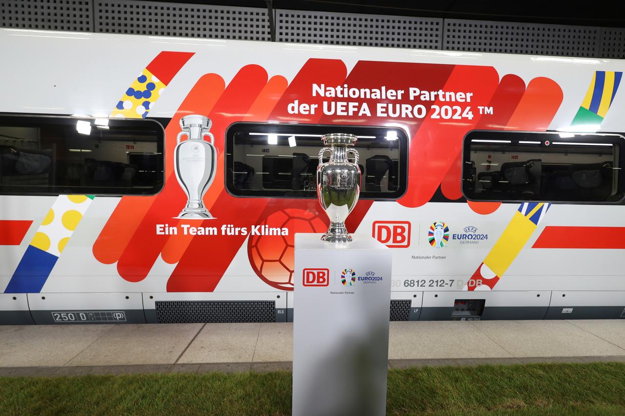 Ein Zug der Deutschen Bahn ist mit dem Schriftzug "Nationaler Partner der UEFA Euro 2024" beklebt, davor steht der Pokal auf einem Podest.