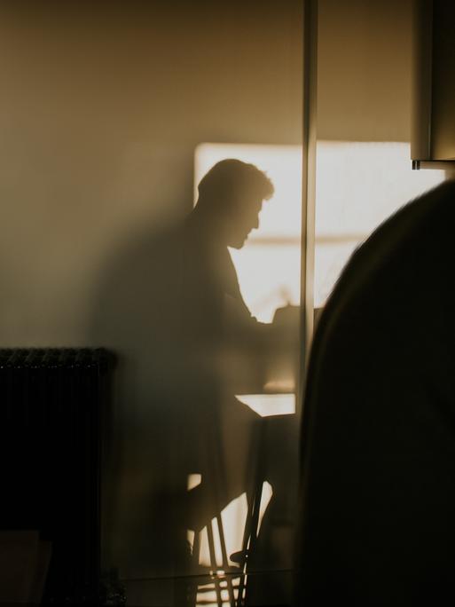 Der Schatten einer männlich gelesenen Person bildet sich an einer Wand ab. Der Schatten einer männlich gelesenen Person bildet sich an einer Wand ab.