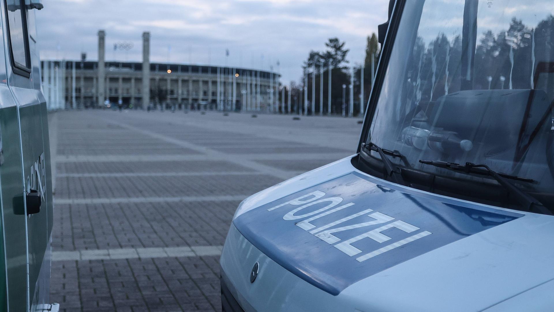Zu sehen ist der vordere Teil eines Polizeiwagens, im Hintergrund ist das Olympiastadion in Berlin zu sehen. 