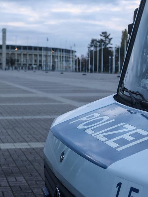 Zu sehen ist der vordere Teil eines Polizeiwagens, im Hintergrund ist das Olympiastadion in Berlin zu sehen. 
