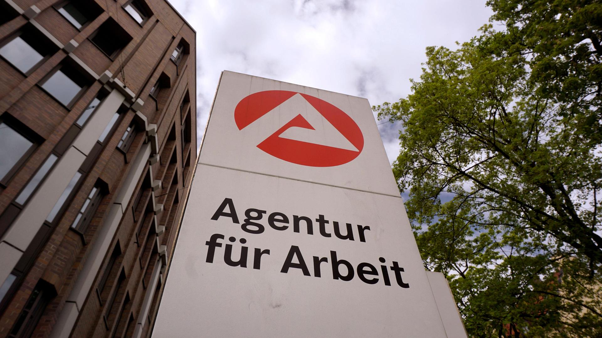 Ein Schild mit der Aufschrift Agentur für Arbeit steht vor einem Gebäude und zeigt in den Himmel